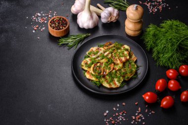 Siyah bir tabakta baharat ve otlarla birlikte koyu beton bir zemin üzerinde leziz ızgara patates dilimleri. Evde yemek pişirmek.