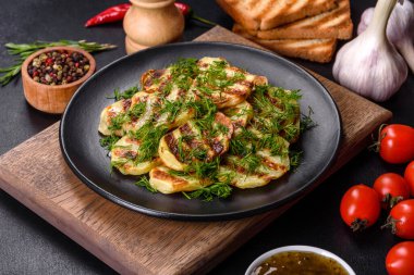 Siyah bir tabakta baharat ve otlarla birlikte koyu beton bir zemin üzerinde leziz ızgara patates dilimleri. Evde yemek pişirmek.