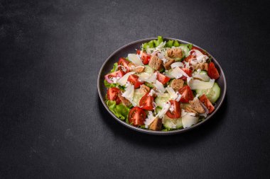 Çeri domatesli taze sebze salatası, salatalık, ekmek kırıntıları ve koyu beton arkaplanda parmesan peyniri.