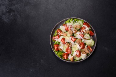 Çeri domatesli taze sebze salatası, salatalık, ekmek kırıntıları ve koyu beton arkaplanda parmesan peyniri.