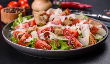 Çeri domatesli taze sebze salatası, salatalık, ekmek kırıntıları ve koyu beton arkaplanda parmesan peyniri.