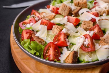 Çeri domatesli taze sebze salatası, salatalık, ekmek kırıntıları ve koyu beton arkaplanda parmesan peyniri.