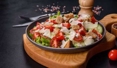 Çeri domatesli taze sebze salatası, salatalık, ekmek kırıntıları ve koyu beton arkaplanda parmesan peyniri.