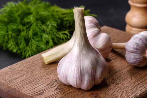 Tahta kesme tahtasının üzerinde koyu beton arka planda duran taze beyaz sarımsak kafalar. Evde yemek pişirmek.