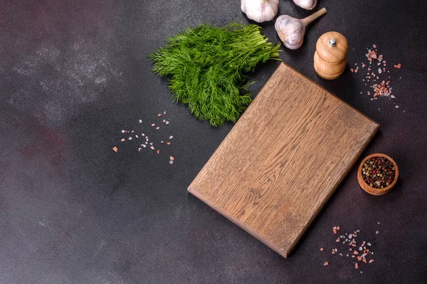 Baharatlar, otlar, kiraz domatesleri ve siyah beton arka planda tuz içeren ahşap bir kesim tahtası. Evde yemek pişirmek.