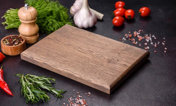 Baharatlar, otlar, kiraz domatesleri ve siyah beton arka planda tuz içeren ahşap bir kesim tahtası. Evde yemek pişirmek.