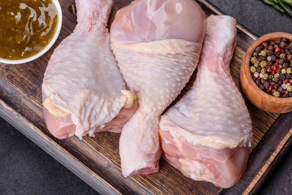 Ahşap bir kesme tahtasının üzerindeki baharatlı ve otlu çiğ tavuğun üç bacağı koyu beton arka planda. Evde yemek pişirmek.