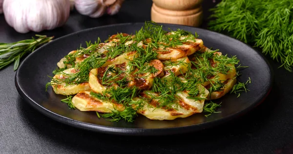 Siyah bir tabakta baharat ve otlarla birlikte koyu beton bir zemin üzerinde leziz ızgara patates dilimleri. Evde yemek pişirmek.