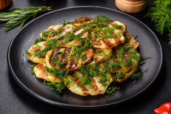 Siyah bir tabakta baharat ve otlarla birlikte koyu beton bir zemin üzerinde leziz ızgara patates dilimleri. Evde yemek pişirmek.