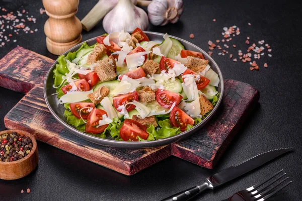 Çeri domatesli taze sebze salatası, salatalık, ekmek kırıntıları ve koyu beton arkaplanda parmesan peyniri.