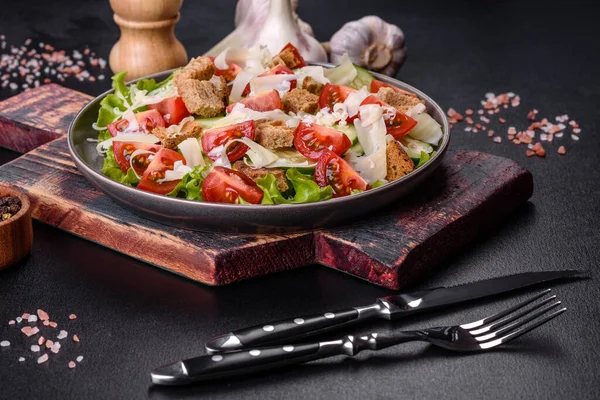 Çeri domatesli taze sebze salatası, salatalık, ekmek kırıntıları ve koyu beton arkaplanda parmesan peyniri.