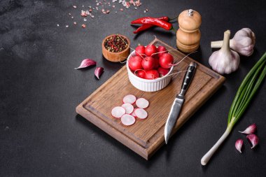 Tahta kesme tahtasında koyu beton zemine karşı bahar salatası yapmak için malzeme olarak lezzetli taze kırmızı turp.