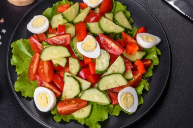 Marul, salatalık, ıspanak, domates ve bıldırcın yumurtası otlu salata ve siyah bir tabakta limon.