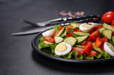 Marul, salatalık, ıspanak, domates ve bıldırcın yumurtası otlu salata ve siyah bir tabakta limon.