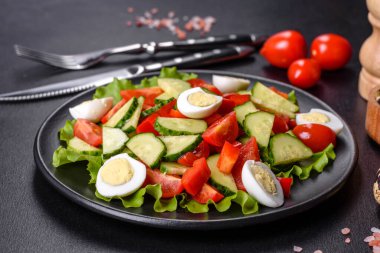 Marul, salatalık, ıspanak, domates ve bıldırcın yumurtası otlu salata ve siyah bir tabakta limon.