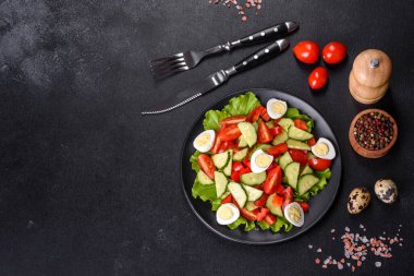 Marul, salatalık, ıspanak, domates ve bıldırcın yumurtası otlu salata ve siyah bir tabakta limon.