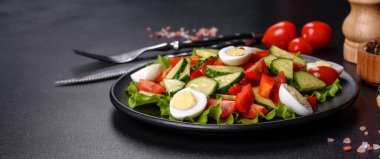 Marul, salatalık, ıspanak, domates ve bıldırcın yumurtası otlu salata ve siyah bir tabakta limon.