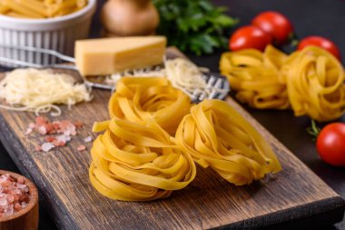 Çiğ tagliatelle macunu, rendelenmiş peynir, kiraz domatesleri, baharatlar ve otlar ahşap kesim tahtasının üzerinde koyu beton bir arka planda.