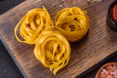 Çiğ tagliatelle macunu, rendelenmiş peynir, kiraz domatesleri, baharatlar ve otlar ahşap kesim tahtasının üzerinde koyu beton bir arka planda.