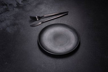 Siyah arka planda boş siyah plaka, çatal ve bıçak. Üst görünüm, alanı kopyala