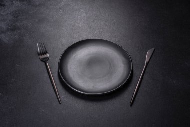 Siyah arka planda boş siyah plaka, çatal ve bıçak. Üst görünüm, alanı kopyala