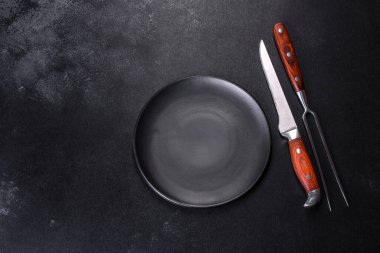 Siyah arka planda boş siyah plaka, çatal ve bıçak. Üst görünüm, alanı kopyala