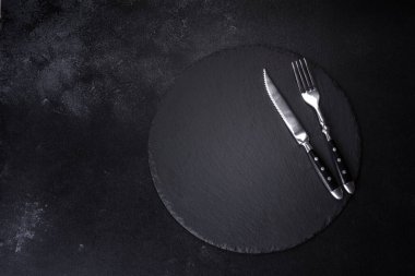 Siyah arka planda boş siyah plaka, çatal ve bıçak. Üst görünüm, alanı kopyala