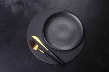 Siyah arka planda boş siyah plaka, çatal ve bıçak. Üst görünüm, alanı kopyala