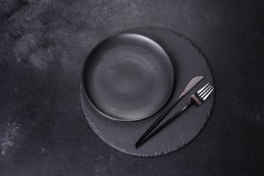 Siyah arka planda boş siyah plaka, çatal ve bıçak. Üst görünüm, alanı kopyala