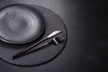 Siyah arka planda boş siyah plaka, çatal ve bıçak. Üst görünüm, alanı kopyala