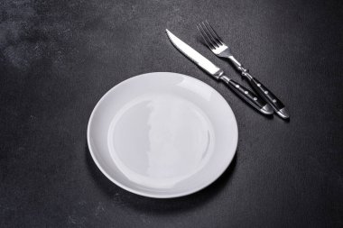 Siyah arka planda boş beyaz tabaklar, çatal ve bıçak. Üst görünüm, alanı kopyala