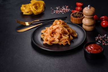Domates soslu ve parmesanlı lezzetli makarna tagliatelle spagettisi. Koyu beton bir masada, siyah bir tabakta servis edilmiş.