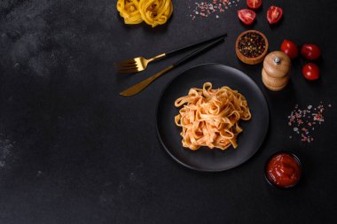 Domates soslu ve parmesanlı lezzetli makarna tagliatelle spagettisi. Koyu beton bir masada, siyah bir tabakta servis edilmiş.