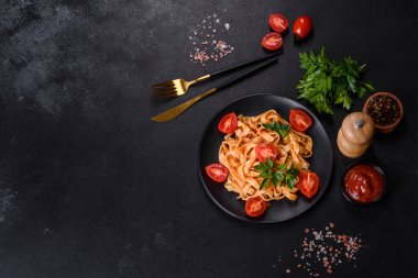 Domates soslu ve parmesanlı lezzetli makarna tagliatelle spagettisi. Koyu beton bir masada, siyah bir tabakta servis edilmiş.