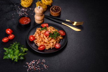 Domates soslu ve parmesanlı lezzetli makarna tagliatelle spagettisi. Koyu beton bir masada, siyah bir tabakta servis edilmiş.