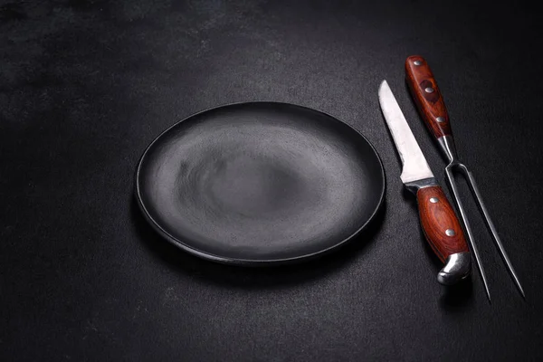 Siyah arka planda boş siyah plaka, çatal ve bıçak. Üst görünüm, alanı kopyala