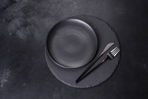 Siyah arka planda boş siyah plaka, çatal ve bıçak. Üst görünüm, alanı kopyala