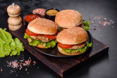 Üç hamburger sığır eti burger ve koyu arka plan üzerinde taze sebze ile. Lezzetli yemekler
