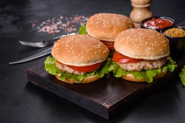 Üç hamburger sığır eti burger ve koyu arka plan üzerinde taze sebze ile. Lezzetli yemekler