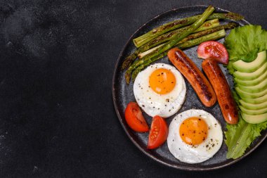Yağda yumurta, sosis, kuşkonmaz, domates, avokado, baharat ve bitkilerle besleyici lezzetli bir kahvaltı. Güne enerjik bir başlangıç için uygun beslenme