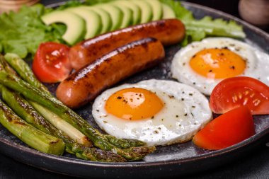 Yağda yumurta, sosis, kuşkonmaz, domates, avokado, baharat ve bitkilerle besleyici lezzetli bir kahvaltı. Güne enerjik bir başlangıç için uygun beslenme