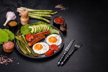 Yağda yumurta, sosis, kuşkonmaz, domates, avokado, baharat ve bitkilerle besleyici lezzetli bir kahvaltı. Güne enerjik bir başlangıç için uygun beslenme