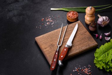 Çatal, bıçak, baharat ve otlar, koyu beton arka planda kesim tahtası. Evde yemek pişirmek.