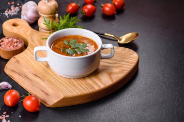 Baharatlı ve maydanozlu taze domates çorbası ahşap bir tahtanın üzerinde koyu beton bir arka planda beyaz bir kasede.