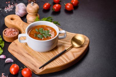 Baharatlı ve maydanozlu taze domates çorbası ahşap bir tahtanın üzerinde koyu beton bir arka planda beyaz bir kasede.