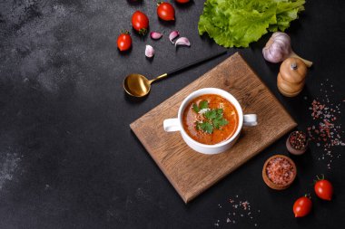 Baharatlı ve maydanozlu taze domates çorbası ahşap bir tahtanın üzerinde koyu beton bir arka planda beyaz bir kasede.