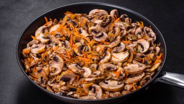 Koyu beton arka planda tavada havuçlu, soğanlı ve baharatlı kızarmış şampiyonlar. Vejetaryen mutfağı