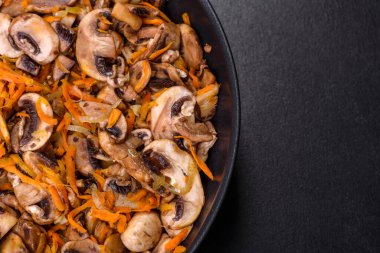 Koyu beton arka planda tavada havuçlu, soğanlı ve baharatlı kızarmış şampiyonlar. Vejetaryen mutfağı