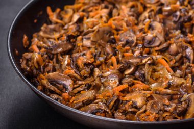 Koyu beton arka planda tavada havuçlu, soğanlı ve baharatlı kızarmış şampiyonlar. Vejetaryen mutfağı