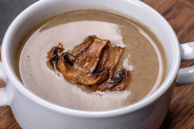 Tahta bir tahtanın üzerinde, üzerinde ekmek kırıntıları, baharatlar ve otlarla birlikte koyu beton bir zemin üzerinde taze, lezzetli bir mantar püresi çorbası. Vejetaryen mutfağı